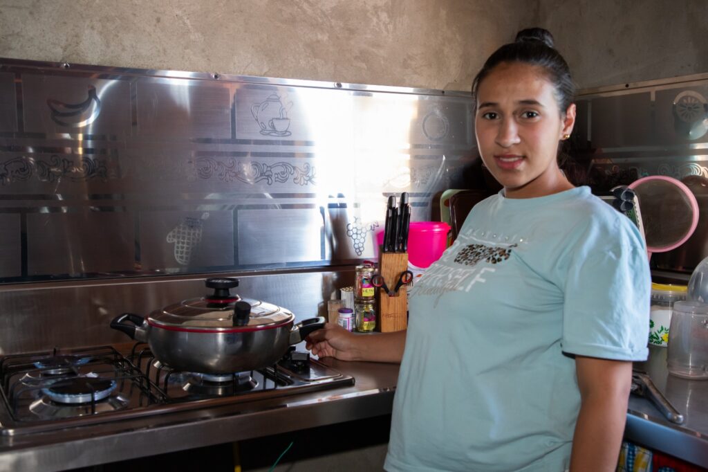 Mujer joven en su cocina de Medellín sonriendo mientras utiliza una estufa de gas natural recién instalada.