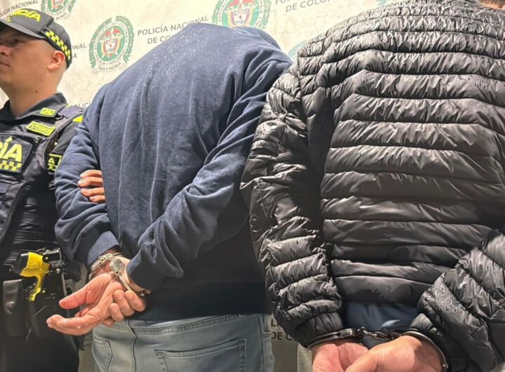Dos hombres esposados y de espaldas custodiados por un agente de la Policía Nacional de Colombia tras ser capturados por robo de joyas en El Poblado.