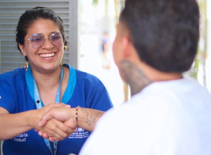 Una profesional de la Secretaría con uniforme azul sonríe mientras estrecha la mano de un ciudadano