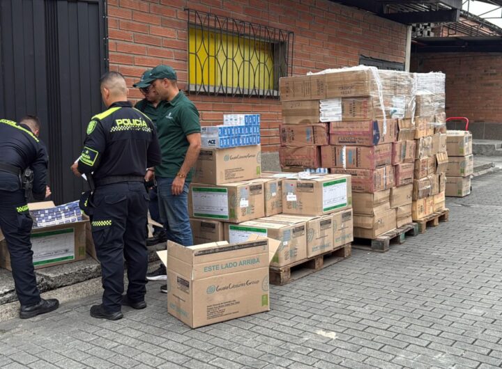 Oficiales de la Policía Nacional de Colombia inspeccionando cajas de cartón con cajetillas de cigarrillos incautadas en una calle de Medellín.