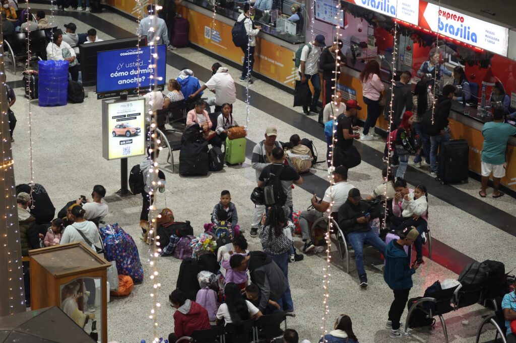 Vista elevada de la sala de espera en la Terminal de Transporte de Medellín, mostrando viajeros con equipaje y decoraciones navideñas de luces.