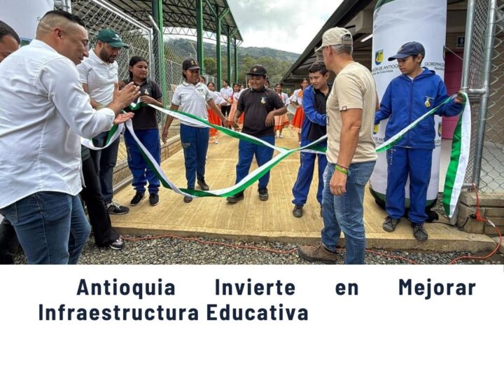 Grupo de personas, incluyendo funcionarios y estudiantes, cortando una cinta verde y blanca en la inauguración de mejoras en infraestructura educativa en Antioquia, con fondo de instalaciones escolares y montañas