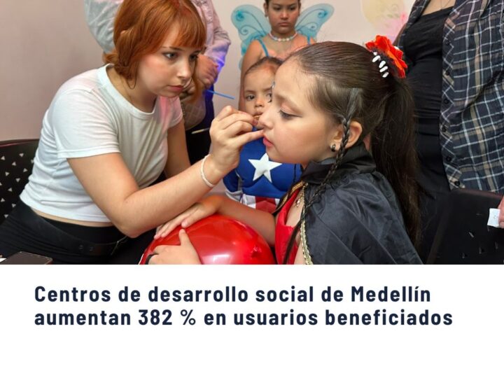 Voluntaria pintando la cara a una niña disfrazada en actividad recreativa de un centro de desarrollo social en Medellín, con otros niños al fondo.
