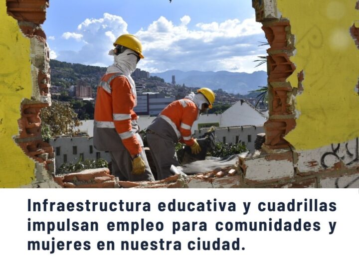Trabajadores con cascos amarillos y uniformes naranjas realizando labores de construcción en una estructura dañada con vista panorámica a la ciudad de Medellín y montañas, promoviendo infraestructura educativa y empleo para comunidades y mujeres.