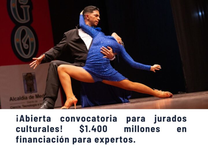 Pareja de bailarines profesionales en intensa pose de baile latino en escenario, con vestuario brillante azul y negro, durante evento cultural en Medellín.