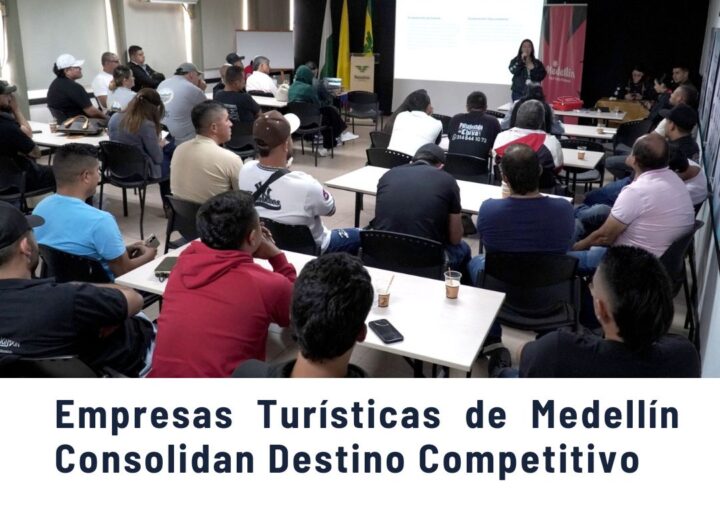 Grupo de empresarios y participantes en una capacitación turística en una sala de Medellín, atentos a una presentación en proyector sobre fortalecimiento empresarial, con banderas de Colombia y Medellín al fondo, promoviendo el sector turístico competitivo de la ciudad.
