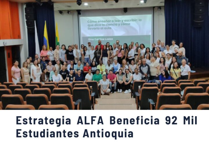 Grupo numeroso de docentes y profesionales de la educación posando en un auditorio de Medellín, sonrientes frente a una pantalla con la ponencia "Cómo enseñar a leer y escribir: lo que dice la ciencia y cómo llevarlo al aula" de Gina Catalina Loaiza, en evento de la estrategia ALFA para alfabetización inicial.
