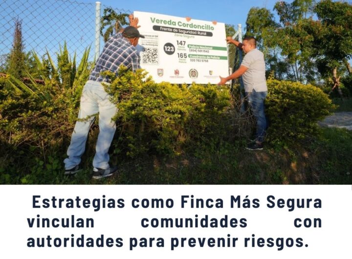 Dos hombres instalando un cartel de seguridad rural en la Vereda Cordoncillo, Frente Cordoncillo 147, como parte de la estrategia Finca Más Segura en las Comunas de Medellín para vincular comunidades con autoridades y prevenir riesgos.