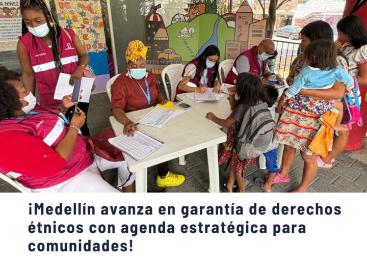 Personas de comunidades étnicas en una jornada de atención y registro en una comuna de Medellín, con personal de chalecos rojos atendiendo a familias, representando la garantía de derechos étnicos.