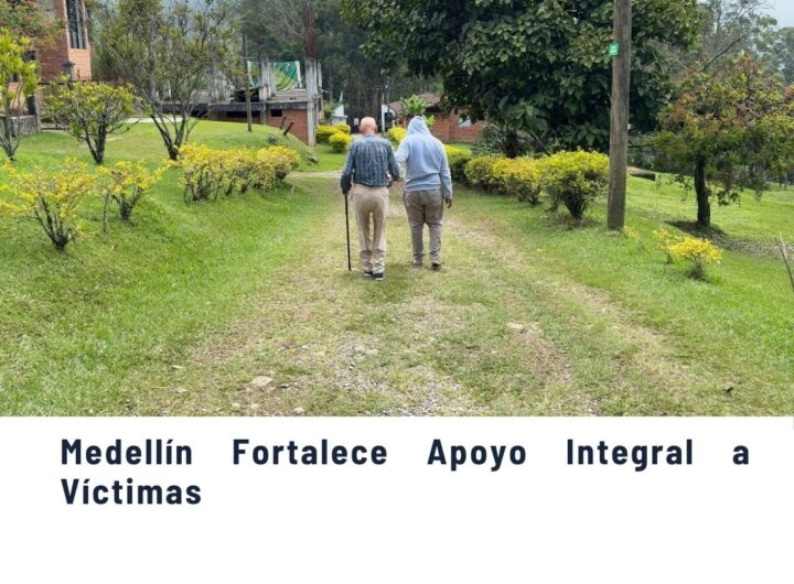 Dos personas mayores caminando por un sendero verde rodeado de arbustos amarillos y vegetación, en un paisaje rural de Medellín, ilustrando el fortalecimiento del apoyo integral a víctimas.