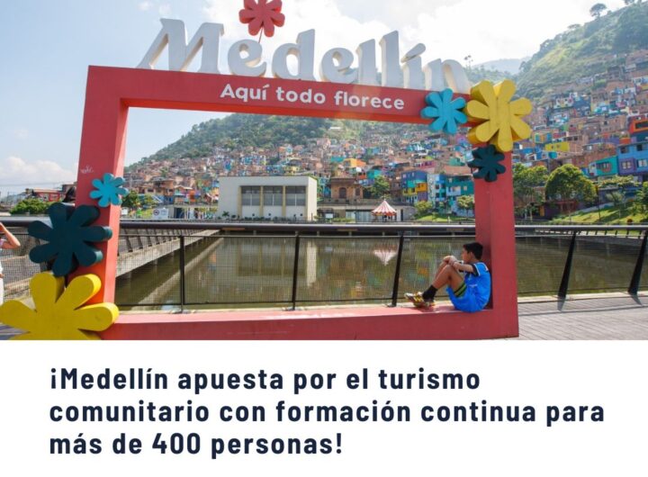 Vista icónica de Medellín con el letrero "Medellín Aquí todo florece" enmarcando la Comuna 13, barrio colorido y transformado, simbolizando el turismo comunitario y el orgullo local.