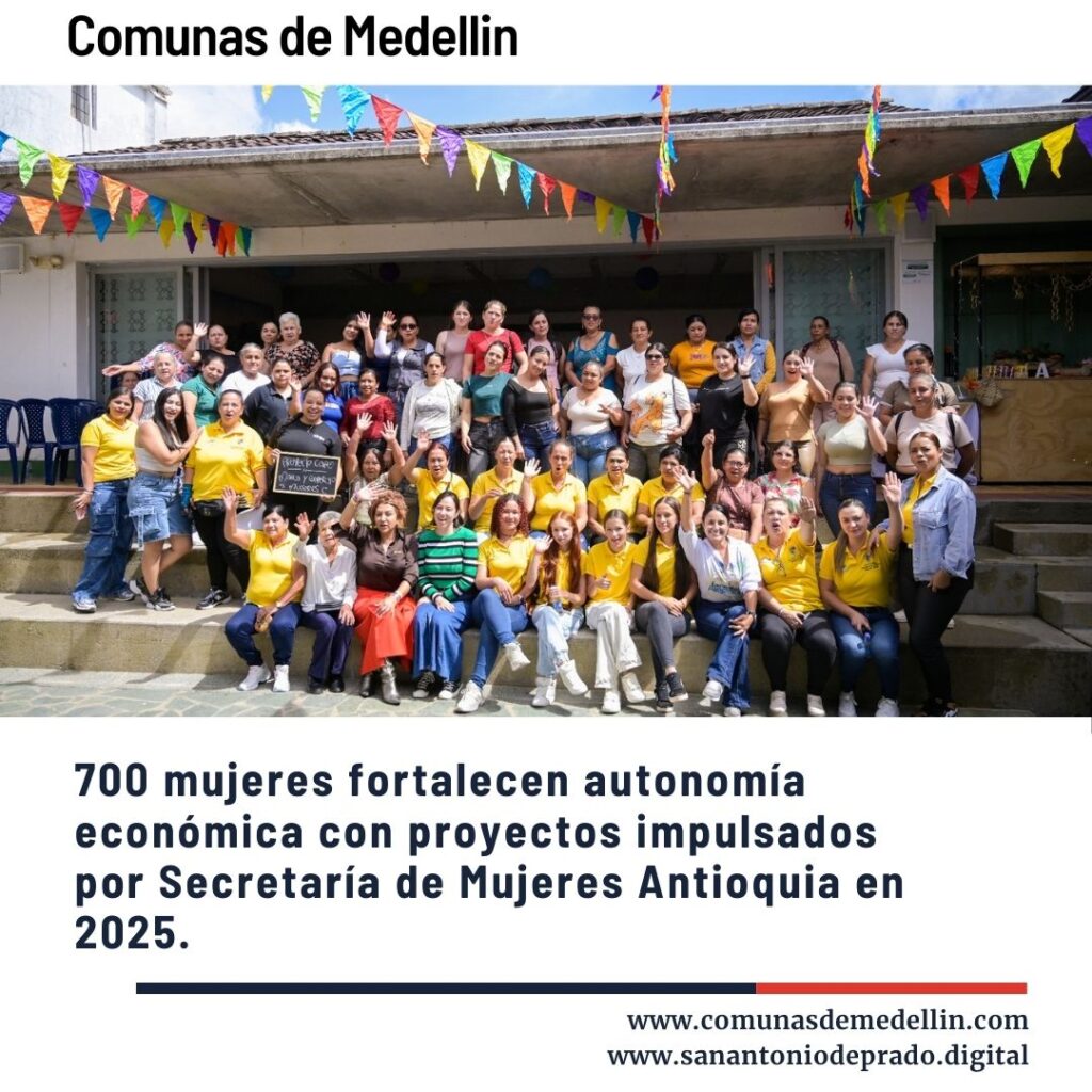 Grupo grande de mujeres sonrientes posando en escaleras al aire libre con banderas de colores, celebrando el fortalecimiento de la autonomía económica de 700 mujeres en Antioquia durante 2025 por la Secretaría de Mujeres.
