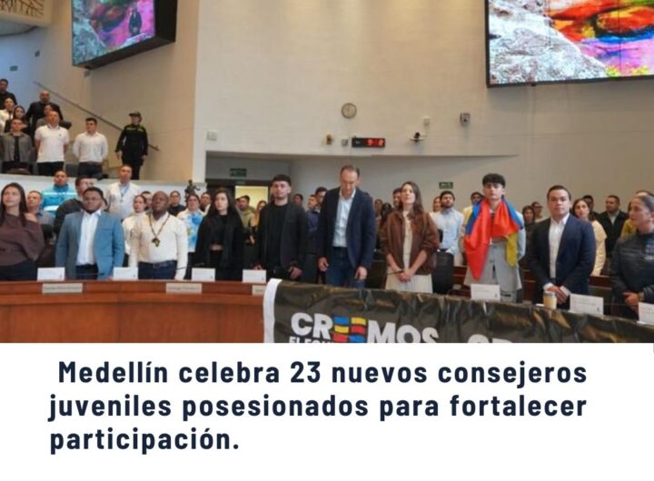 Ceremonia de posesión de 23 nuevos consejeros juveniles en Medellín, grupo en tarima con banderas y público en auditorio, fortaleciendo participación juvenil - Comunas de Medellín.