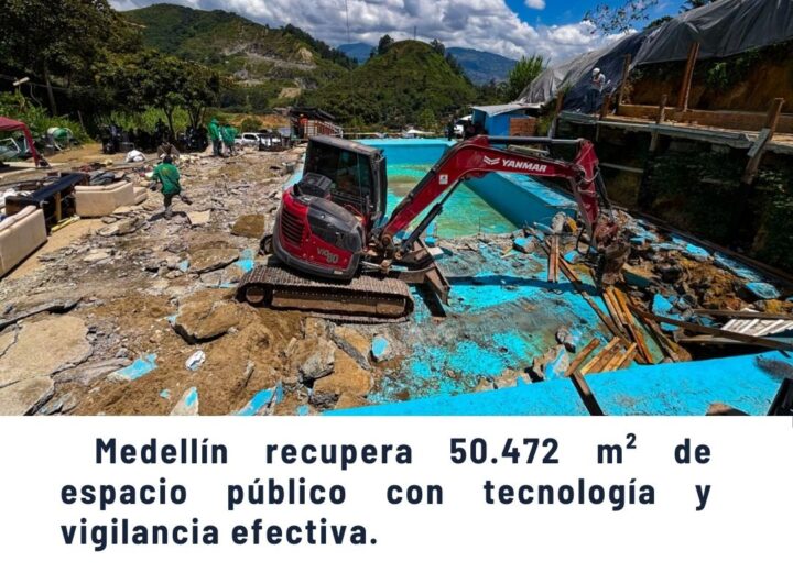 Escena de recuperación de espacio público en Medellín con excavadora Yanmar demoliendo estructura azul, trabajadores en sitio montañoso, texto 'Medellín recupera 50.472 m² de espacio público con tecnología y vigilancia efectiva' - Comunas de Medellín.