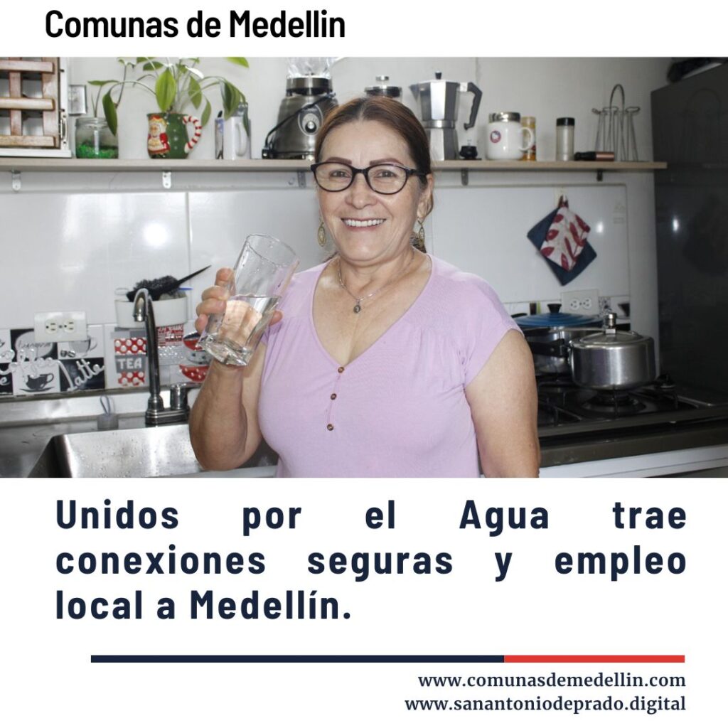 Mujer sonriente sosteniendo un vaso de agua en una cocina, promoviendo el programa Unidos por el Agua que trae conexiones seguras y empleo local a las comunas de Medellín.
